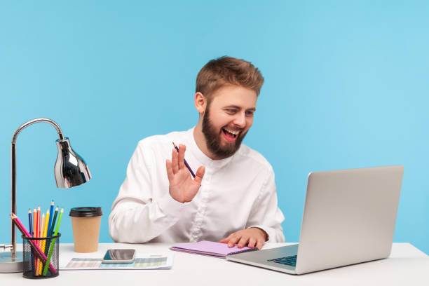 istock Happy smiling man office worker sitting at workplace with notepad and pencil, saying hi talking video call on laptop, holding meeting online, brainstorming 1299249596