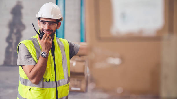 Professional cargo worker talks on portable radio to contact another worker stock photo