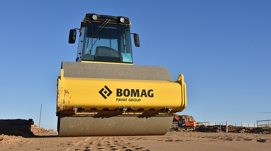 Vibration single-cylinder road roller BOMAG leveling soil at construction site. Soil Compactor on road work project. BELARUS - APRIL 11, 2020