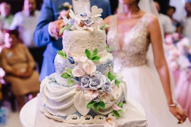 Bride and a groom is cutting their rustic wedding cake on wedding banquet. Hands cut the cake with delicate flowers.