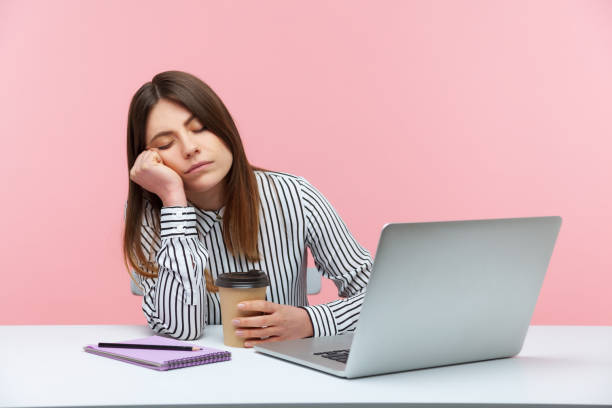 assonna inefficiente donna impiegato che sonnecchia appoggiata alla testa e tiene la tazza di caffè seduta sul posto di lavoro con laptop, esaurimento fisico - one person people boredom isolated foto e immagini stock