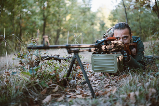 Soldier laying in the forest with machine gun.