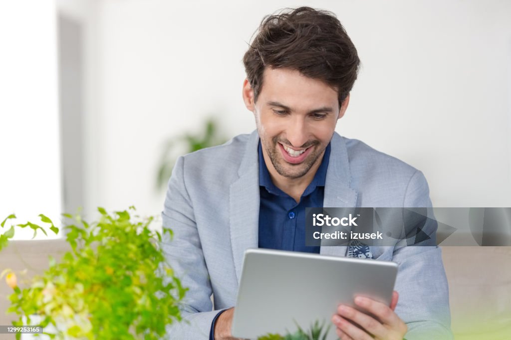 Businessman working in the eco-friendly green office Cheerful mid adult men wearing grey jacket sitting on sofa in the creative workplace and using digital tablet. 30-39 Years Stock Photo