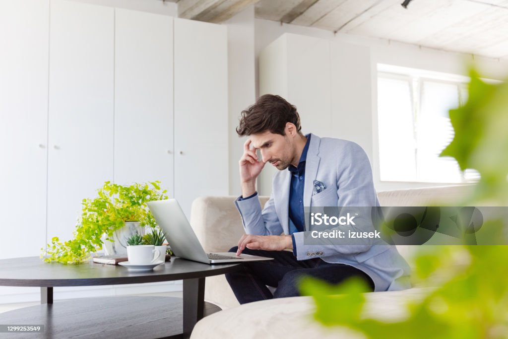 Businessman working on laptop in the green office Thoughtful mid adult men wearing grey jacket sitting on sofa in the creative workplace and using laptop. 30-39 Years Stock Photo
