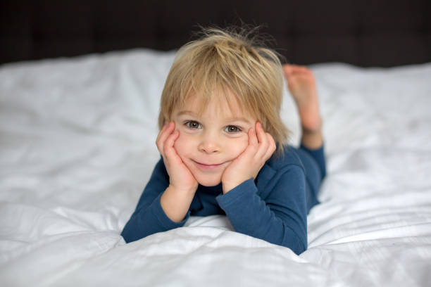 istock Cute child, lying in bed, playing with little stuff toy 1299254552