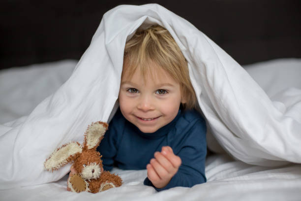 istock Cute child, lying in bed, playing with little stuff toy 1299254570