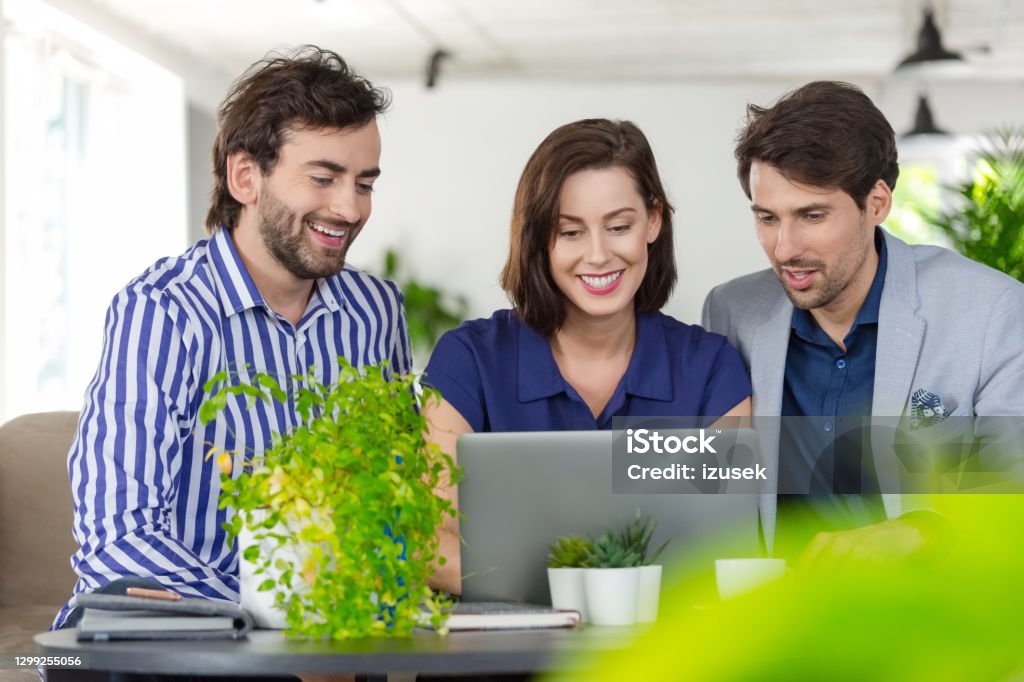 Creative team working in a green office Mid adult women and men sitting on sofa in the creative eco-friendly workplace, working together over laptop. Sustainable Lifestyle Stock Photo Creative team working in a green office Mid adult women and men sitting on sofa in the creative eco-friendly workplace, working together over laptop. Sustainable Lifestyle Stock Photo