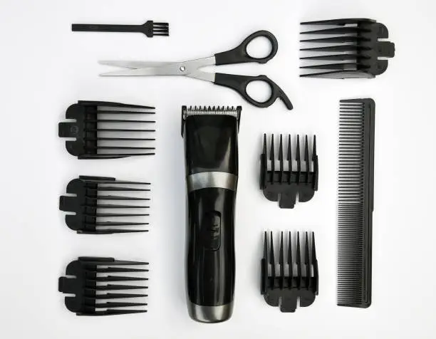 Electric hair clipper, buzz cutters, beard trimer and face shaver. With accessories, scissors, combs and brush. Geometric flat lay against a white background