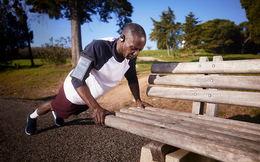 Active senior african-american man doing push ups on park bench outdoors