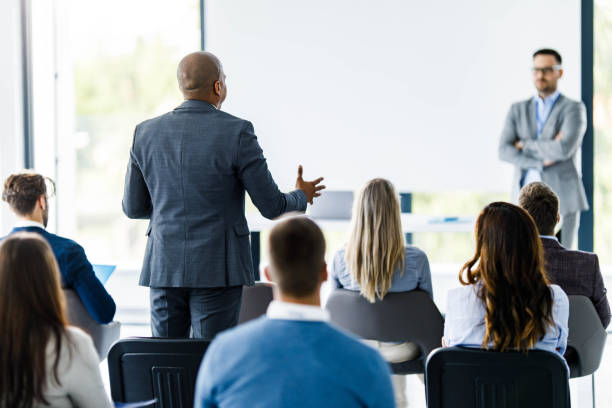 istock Back view of black businessman talking to instructor on a presentation in board room. 1299259394