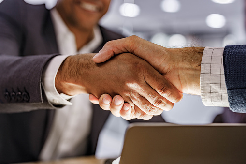 Close up of unrecognizable male entrepreneurs shaking hands after reaching an agreement on a meeting in the office.