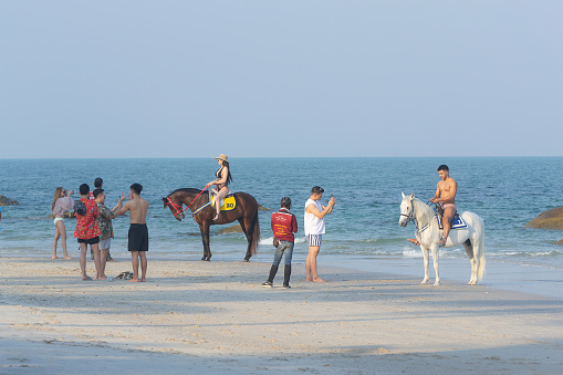 Young people pose for pictures on horseback at Hua Hin Beach, Thailand - January 17, 2021;