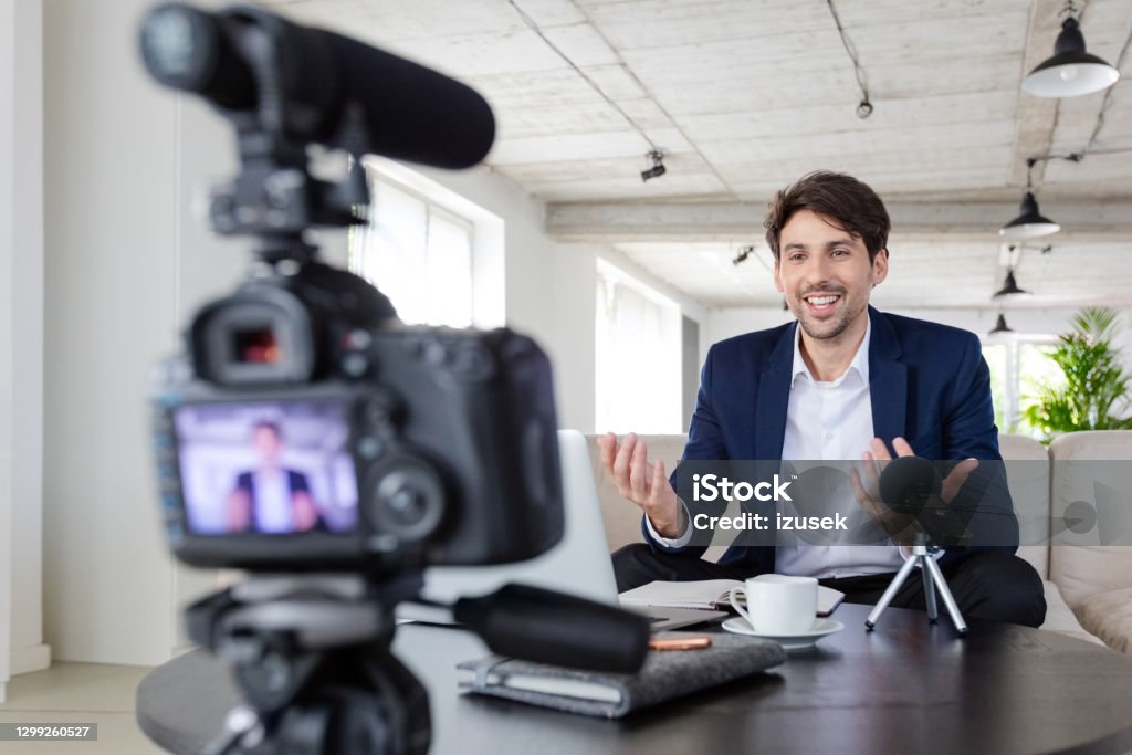 Businessman making a video blog in the office Mid adult businessmen wearing navy blue suit making a video blog. Vlogger recording content on digital camera in the creative office. Influencer Stock Photo