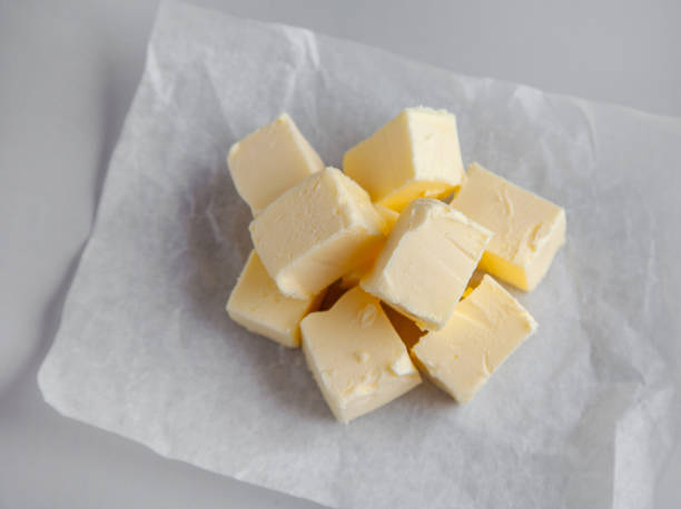 istock pieces of butter on wrapping paper on grey kitchen table background, selective focus 1299261960