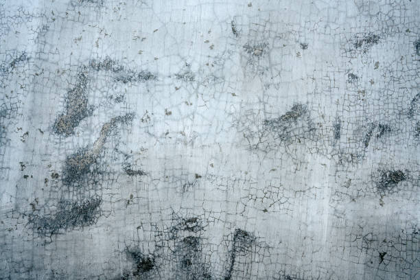 istock White peeling paint on a concrete wall with brownish black patches emerging. 1299265769