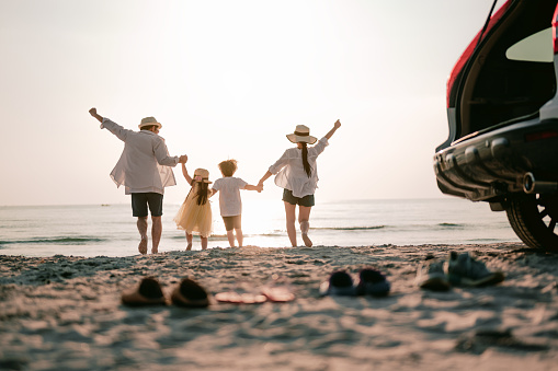 Vacaciones en familia, Feliz familia corriendo en la playa en la puesta de sol. Vista trasera de una familia feliz en una playa tropical y un coche en el lado. photo