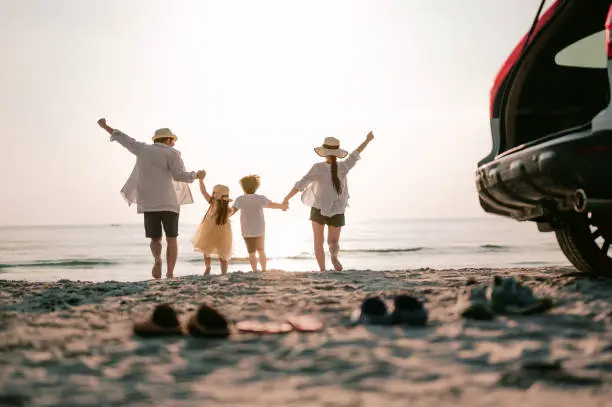 Photo of Family vacation holiday, Happy family running on the beach in the sunset. Back view of a happy family on a tropical beach and a car on the side.