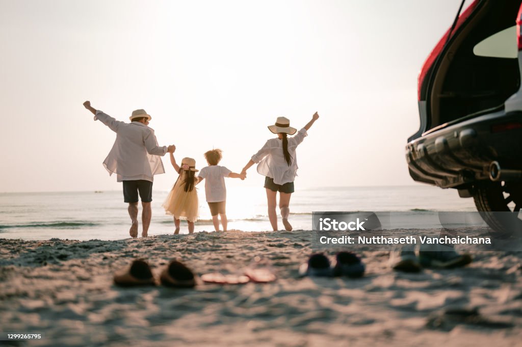 Familjesemester semester, Happy familj som kör på stranden i solnedgången. Tillbaka syn på en lycklig familj på en tropisk strand och en bil på sidan. - Royaltyfri Släkt Bildbanksbilder