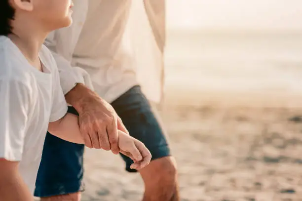Close up on hands.Family vacation holiday, Happy family walking on the beach in the sunset.Father is holding-hands little boy.
