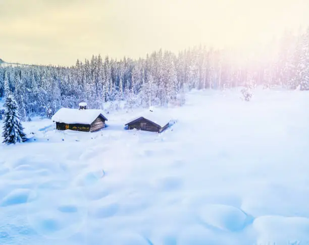 Idyllic mountain log cabin covered in deep snow in a scenic winter sunset in the wild.