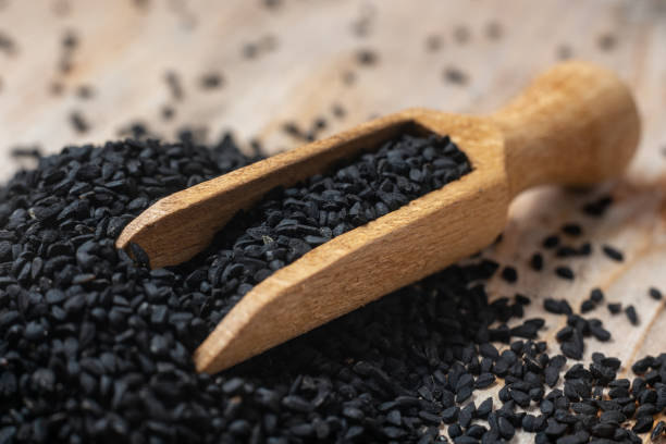 istock Black cumin seeds and wooden scoop, texture background 1299270381