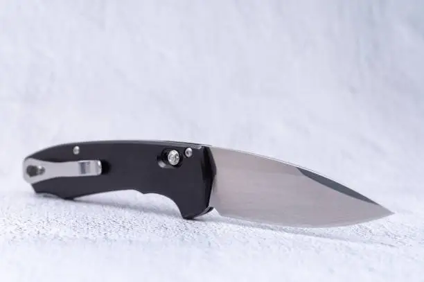 Photo of A knife with a mirror polished blade and a black handle. Knife on a white background. Knife with a clip for carrying.