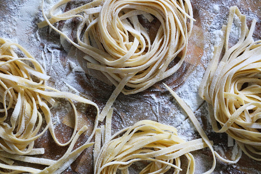 Stock photo showing Italian cuisine. Home made tagliatelle pasta nests left to dry on floured wooden chopping board.