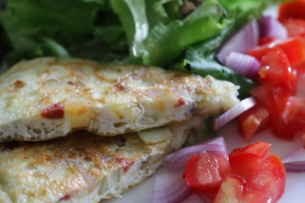 istock Close-up image of Spanish tortilla / frittata on patterned plate, homemade Spanish breakfast omelette in triangle slices with chopped tomato, red onion and lettuce leaves, focus on foreground 1299272760