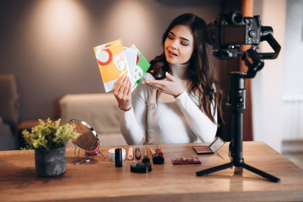 istock Beauty blogger nice female filming daily make-up routine tutorial on camera. Influencer young woman live streaming cosmetics product review in home studio. Vlogger job. Showing makeup and care products 1299275838