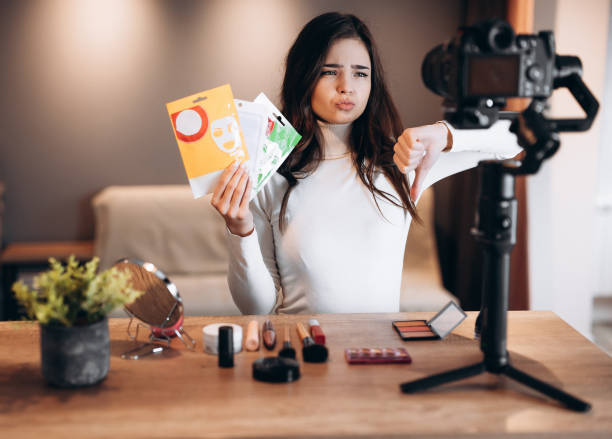 istock Beauty blogger sweet female filming daily make-up routine tutorial on camera. Influencer young woman live streaming cosmetics product review in home studio. Vlogger job. Showing skin-care and beauty products. Dislike. 1299275886