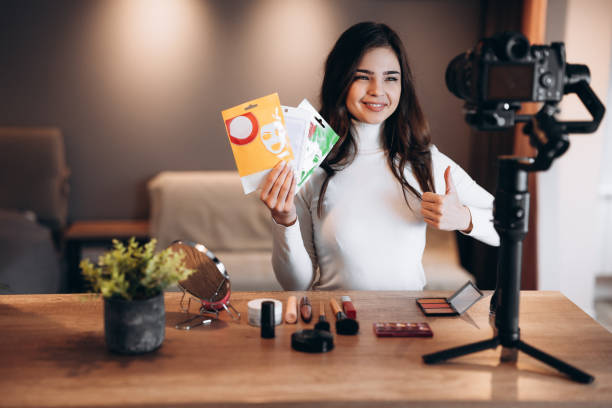istock Beauty blogger nice female filming daily make-up routine tutorial on camera. Influencer young woman live streaming cosmetics product review in home studio. Vlogger job. Showing skin-care and beauty products 1299275889