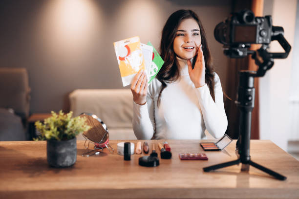 istock Beauty blogger sweet female filming daily make-up routine tutorial on camera. Influencer young woman live streaming cosmetics product review in home studio. Vlogger job. Showing skin-care and beauty products 1299275892