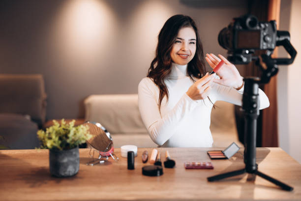 istock Beauty blogger pretty female filming daily make-up routine tutorial on camera. Influencer young woman live streaming cosmetics product review in home studio. Vlogger job. DIY. 1299275898