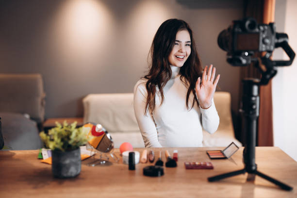 istock Beauty blogger nice female filming daily make-up routine tutorial on camera. Influencer young woman live streaming cosmetics product review in home studio. Vlogger job. DIY putting makeup 1299275914