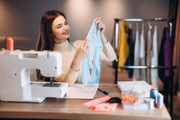 istock Young dressmaker woman with sewing machine. Seamstress checking textile in workshop. Creating online clothing design courses. 1299276030
