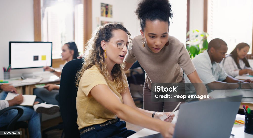 Pairing talent promotes productivity Shot of two young businesswomen using a laptop together in a modern office Project Manager Stock Photo