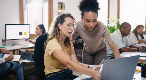 Pairing talent promotes productivity Shot of two young businesswomen using a laptop together in a modern office project manager stock pictures, royalty-free photos & images