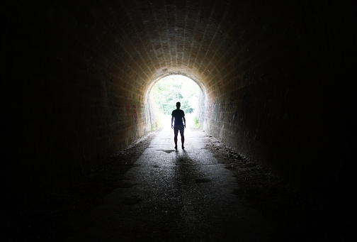 silhouette of man standing in the light at the end of the tunnel