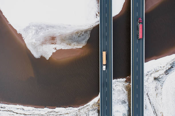 Trucking In Winter Aerial drone view of semi trucks crossing a tidal river. drone point of view road stock pictures, royalty-free photos & images
