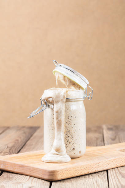 Natural fermented rye sourdough in a jar is on the kitchen board. It flows out. Natural fermented rye sourdough in a jar is on the kitchen board. It flows out. Healthy eating yeast starter stock pictures, royalty-free photos & images