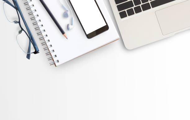 istock Blank paper notebook, laptop computer,glasses and smart phone on white table background. 1299288644