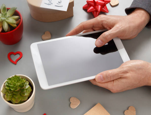istock Hands using tablet near gift boxes and BE MY VALENTINE card 1299291104