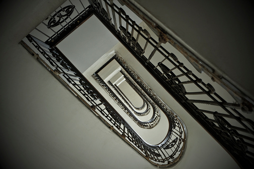 A view from the top, looking down into an industrial building stairwell. Metal stairs and railings lead down several floors into the basement. 