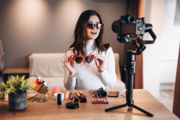 Beauty blogger pretty female in sunglasses filming daily make-up routine tutorial on camera. Influencer young woman live streaming cosmetics product review in home studio. Vlogger job. Holding sunglasses. belleza blogger bonita mujer en gafas de sol filmando daily make-up rutina tutorial en la cámara. influencer joven mujer transmisión en vivo cosméticos revisión de productos en el estudio en casa. trabajo de vlogger. sosteniendo gafas de sol