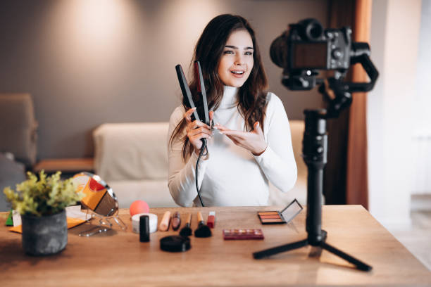 istock Beauty blogger nice female filming daily make-up routine tutorial on camera. Influencer young woman live streaming cosmetics product review in home studio. Vlogger job. DIY putting makeup 1299291422