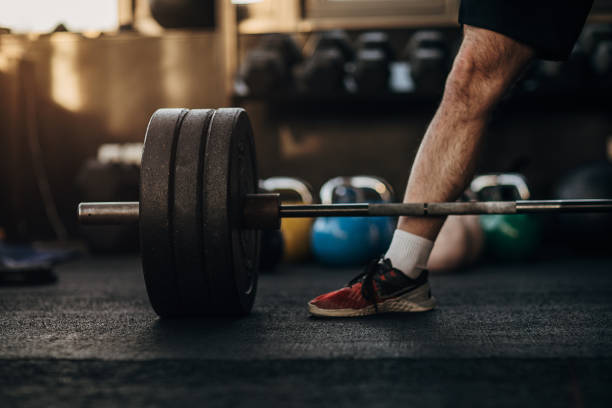 istock Man standing next to barbell with weights in gym 1299291738
