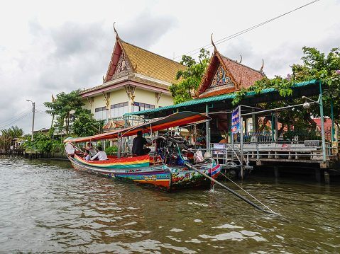 Bangkok, Thailand- August 25, 2018: Colorful canal boat with tourists with a traditional Thai building behind.