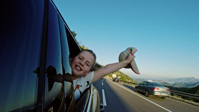 Girl waving hat from car window