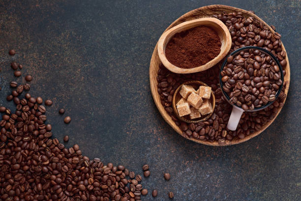 istock Coffee roasted beans in cup and scattered nearby, ground coffee and cane sugar on a brown table background. Top view with space to copy text. 1299300916