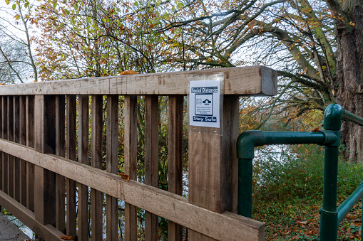 Foot bridge with social distancing sign. Hinchingbrooke Park, Huntingdon, Cambridgeshire, England, UK.